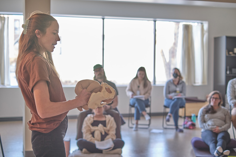 a female educator holding a baby and pelvis in front of a birth class