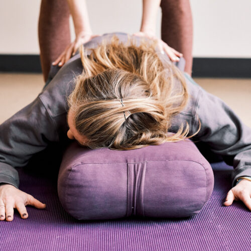 woman doing restorative yin yoga child's pose on a bolster