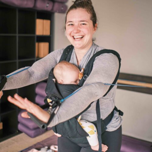 mom working out with exercise bands while wearing an infant