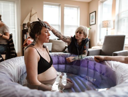 woman in labor sitting in a birth pool with a doula rubbing her forehead with a wet rag