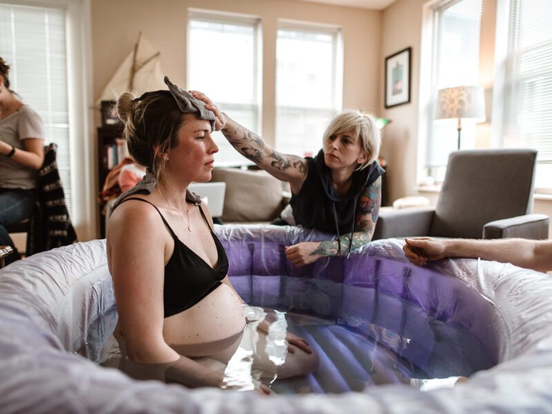 woman in labor sitting in a birth pool with a doula rubbing her forehead with a wet rag