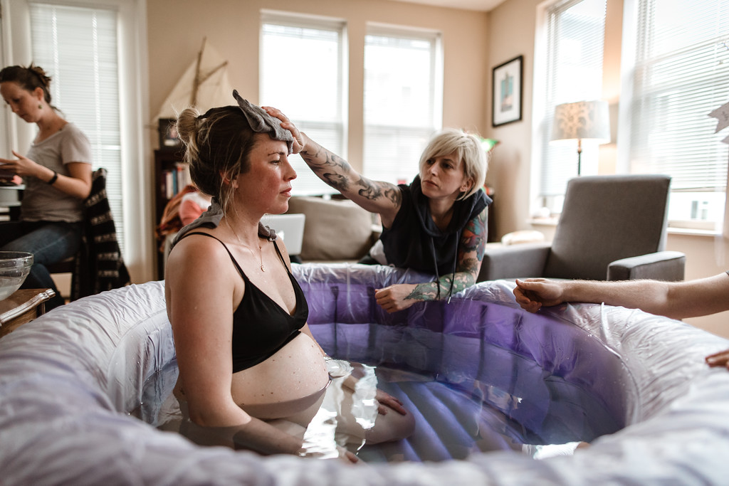 woman in labor sitting in a birth pool with a doula rubbing her forehead with a wet rag