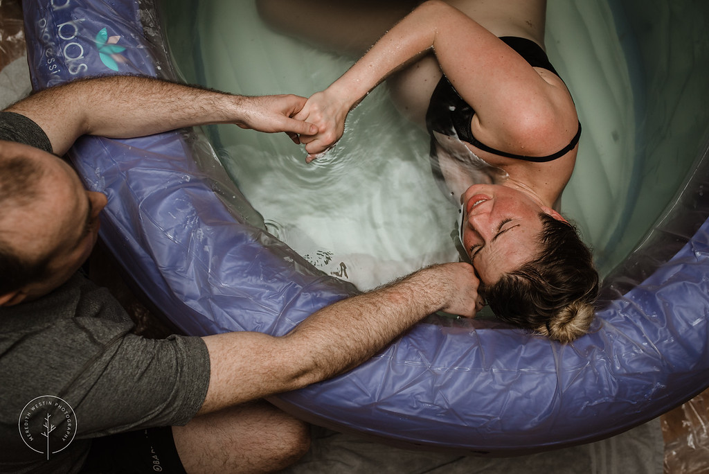 mom in labor in a birthing pool holding dad's hand