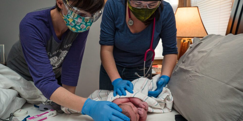 two midwives holding a newly born infant on a table