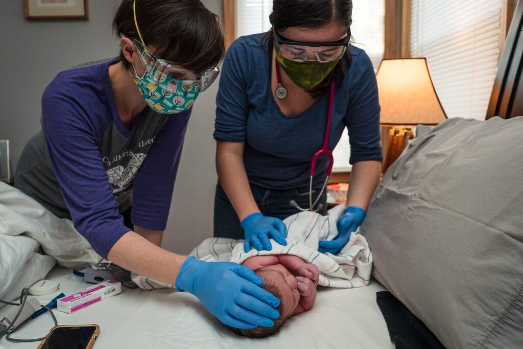 two midwives holding a newly born infant on a table