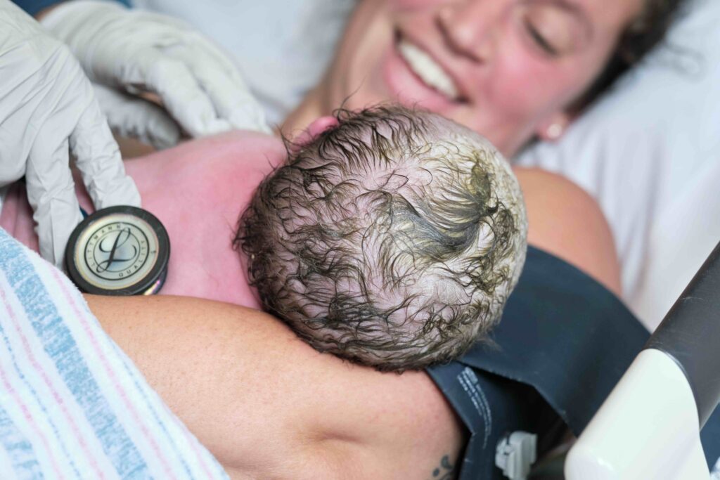 a nurse measures the newborn's heartbeat in the arms of their motherr